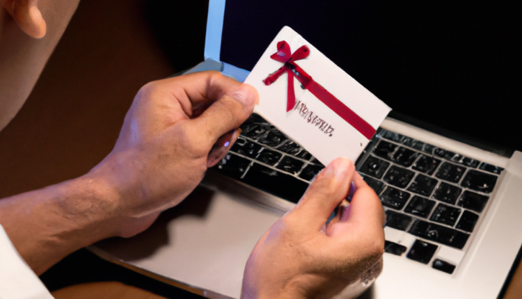 A Gift Card in the hands of a man, who is looking at a MacBook at his desk